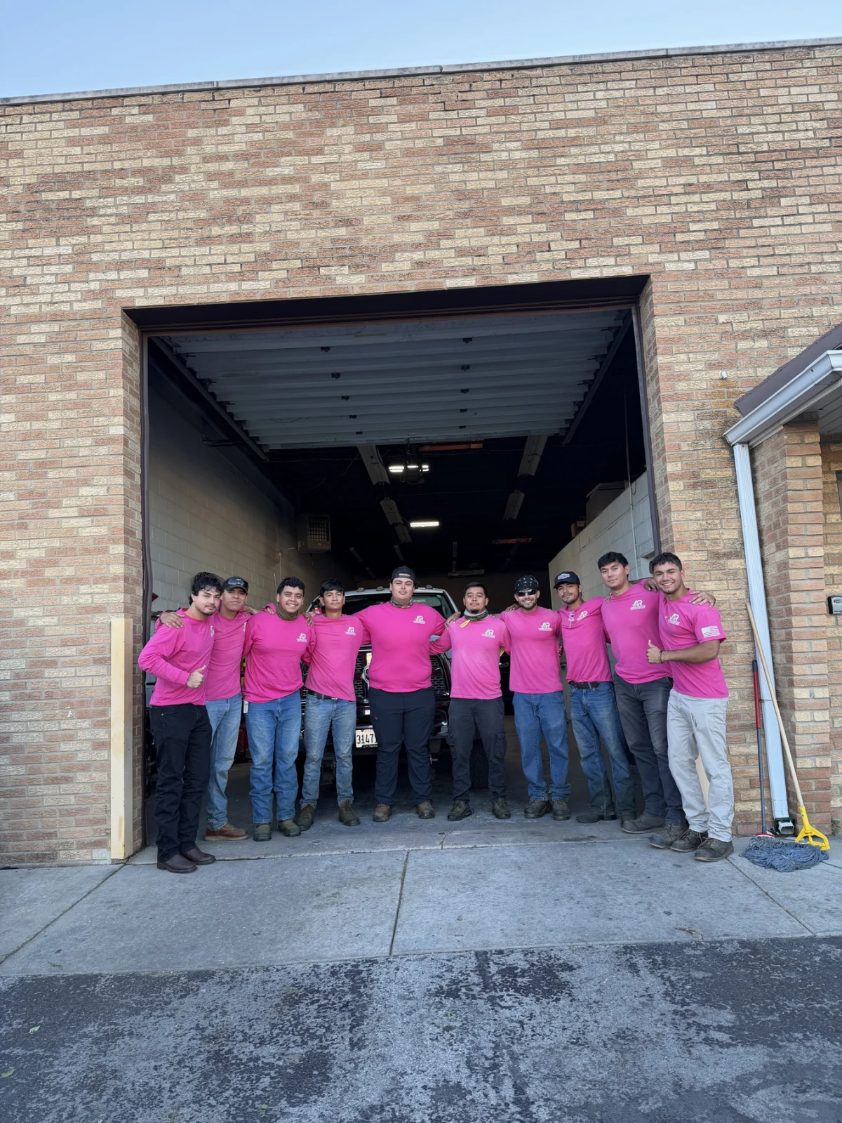 The A.R Lawn Service crew standing together outside the shop in pink company shirts