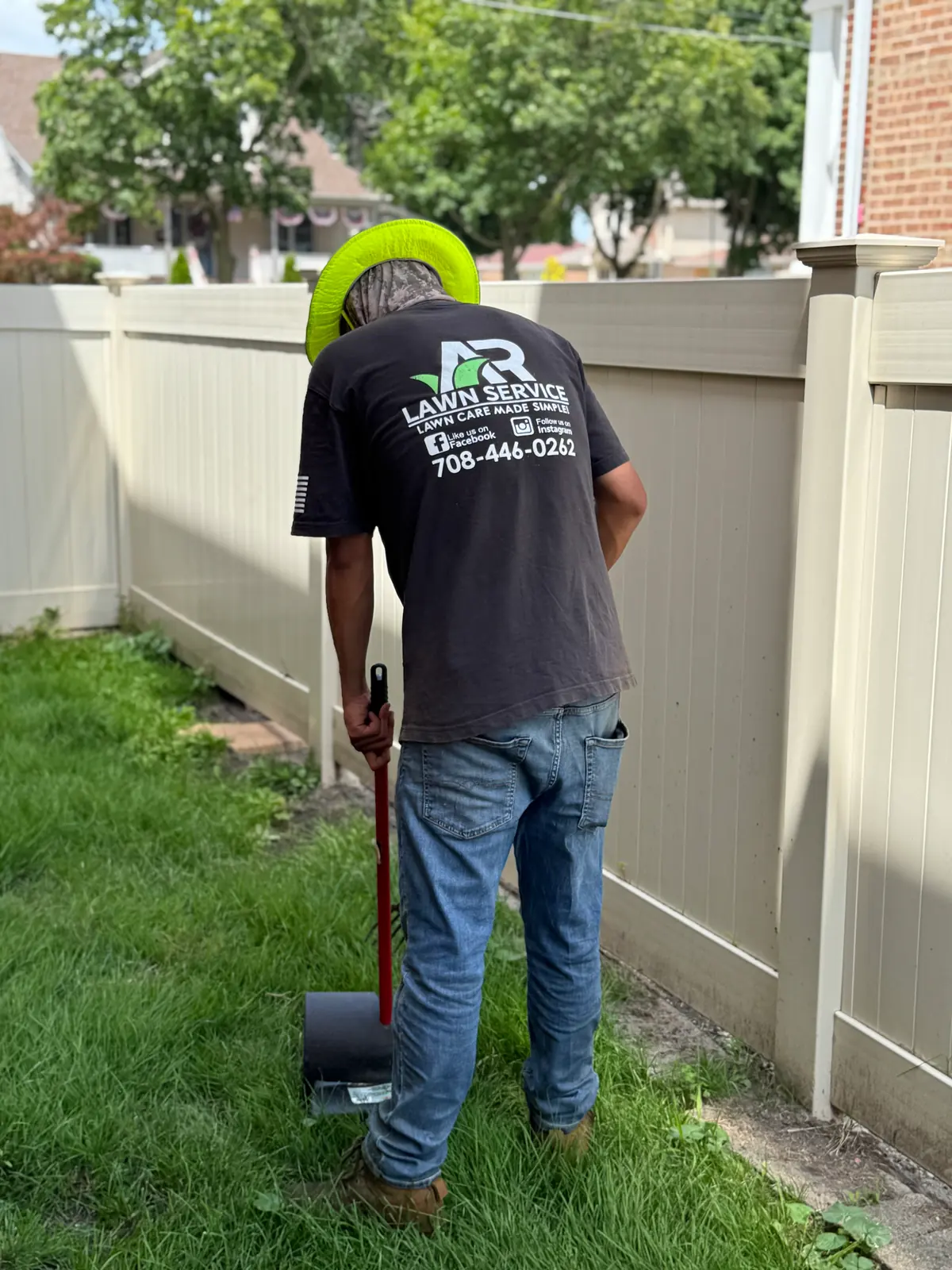 An A.R Lawn Service employee using a scoop to remove dog waste from a fenced backyard