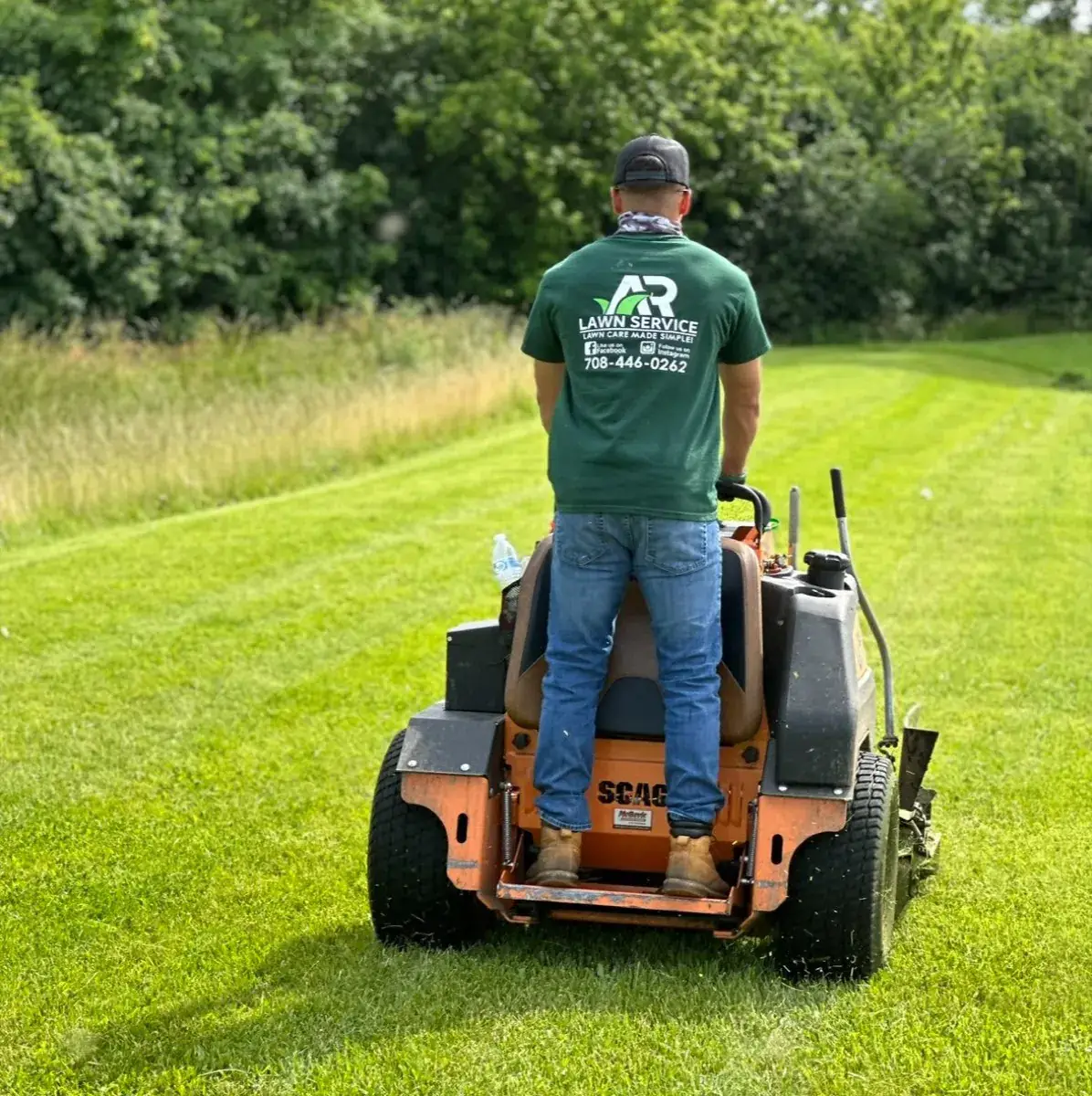 An A.R Lawn Service crew member mowing in a company shirt
